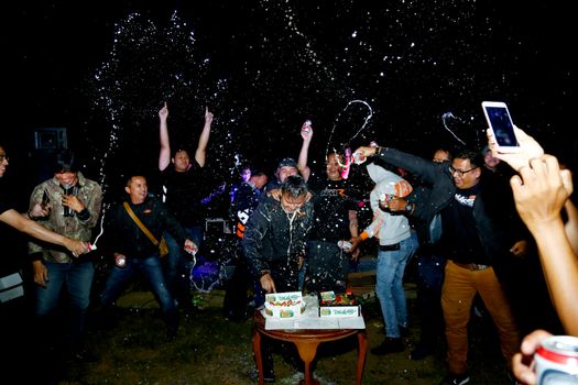 A vibrant night party in West Java with people celebrating with cake and drinks.