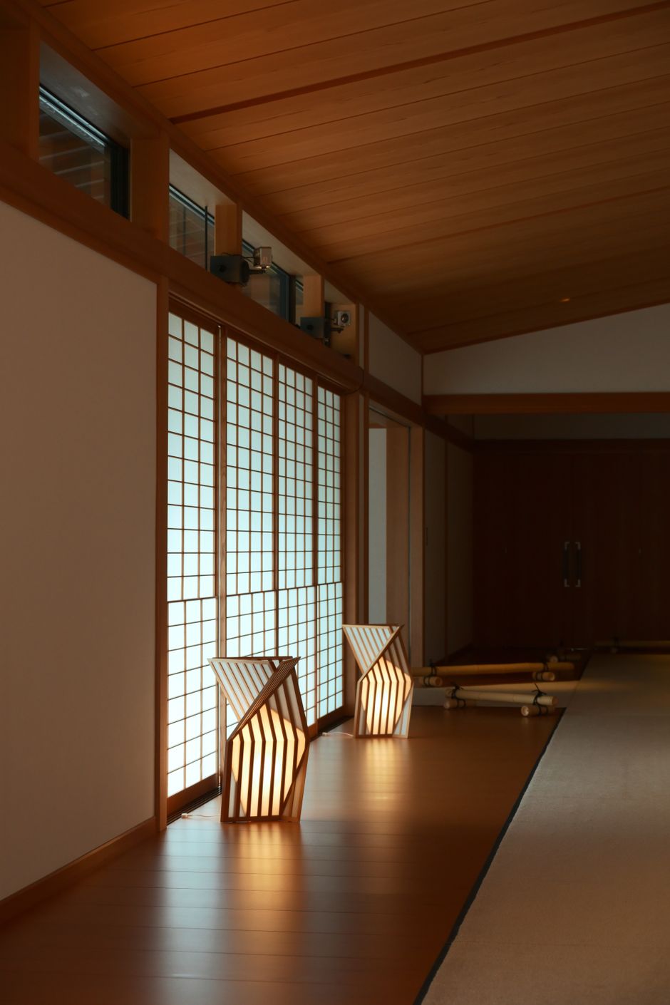 Elegant Japanese room with wooden floor and shōji screens illuminated by modern lanterns.