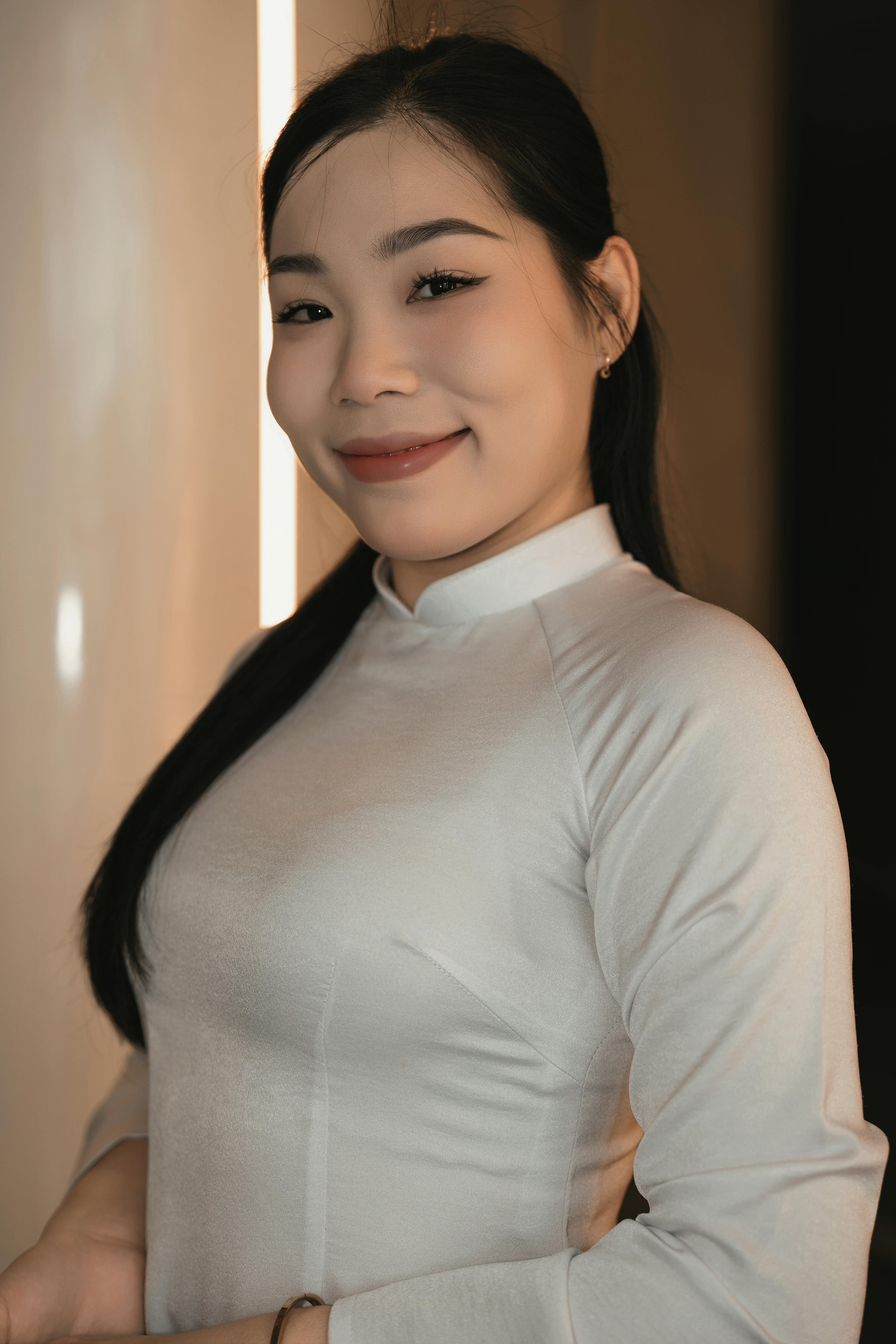 Elegant woman in white traditional dress smiling indoors with soft lighting.