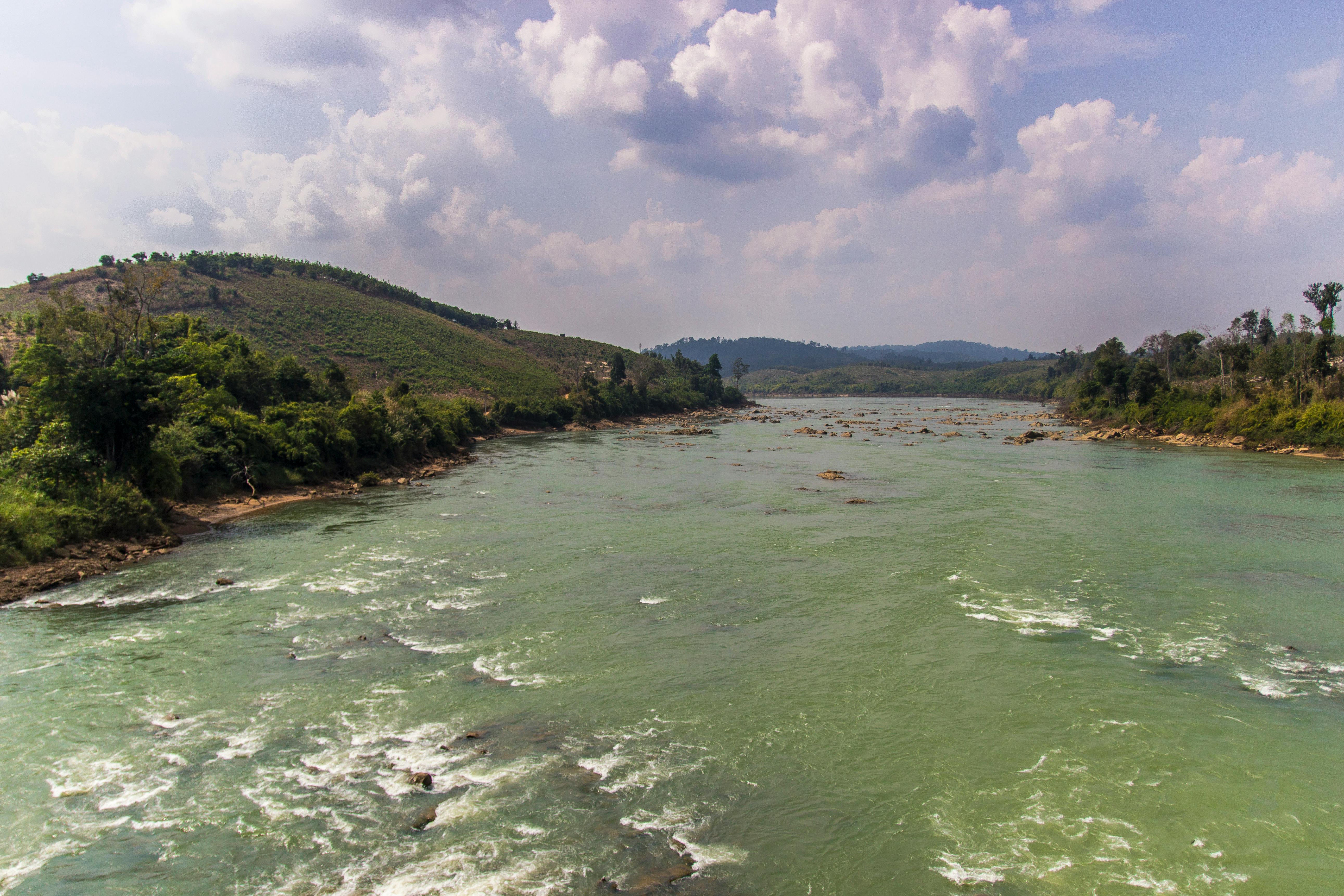 Breathtaking view of a river flowing through Gia Lai, Vietnam surrounded by lush hills and cloudy skies.