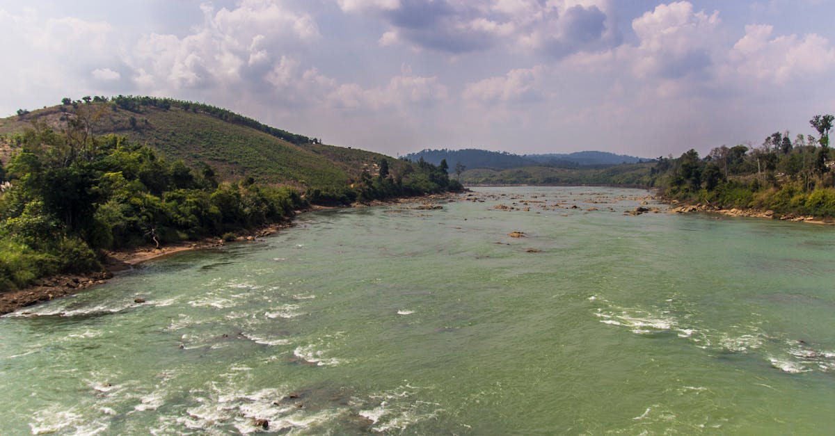 Breathtaking view of a river flowing through Gia Lai, Vietnam surrounded by lush hills and cloudy skies.