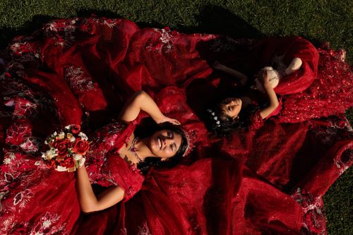 Free Aerial shot of women in vibrant red dresses lying on grass, holding roses. Stock Photo