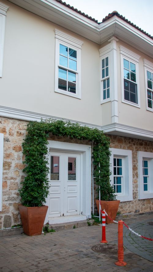 Free A cozy house facade with climbing ivy, large potted plants, and elegant white windows. Stock Photo