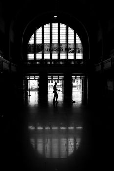A dramatic silhouette of a person in a large indoor hall with arched windows.