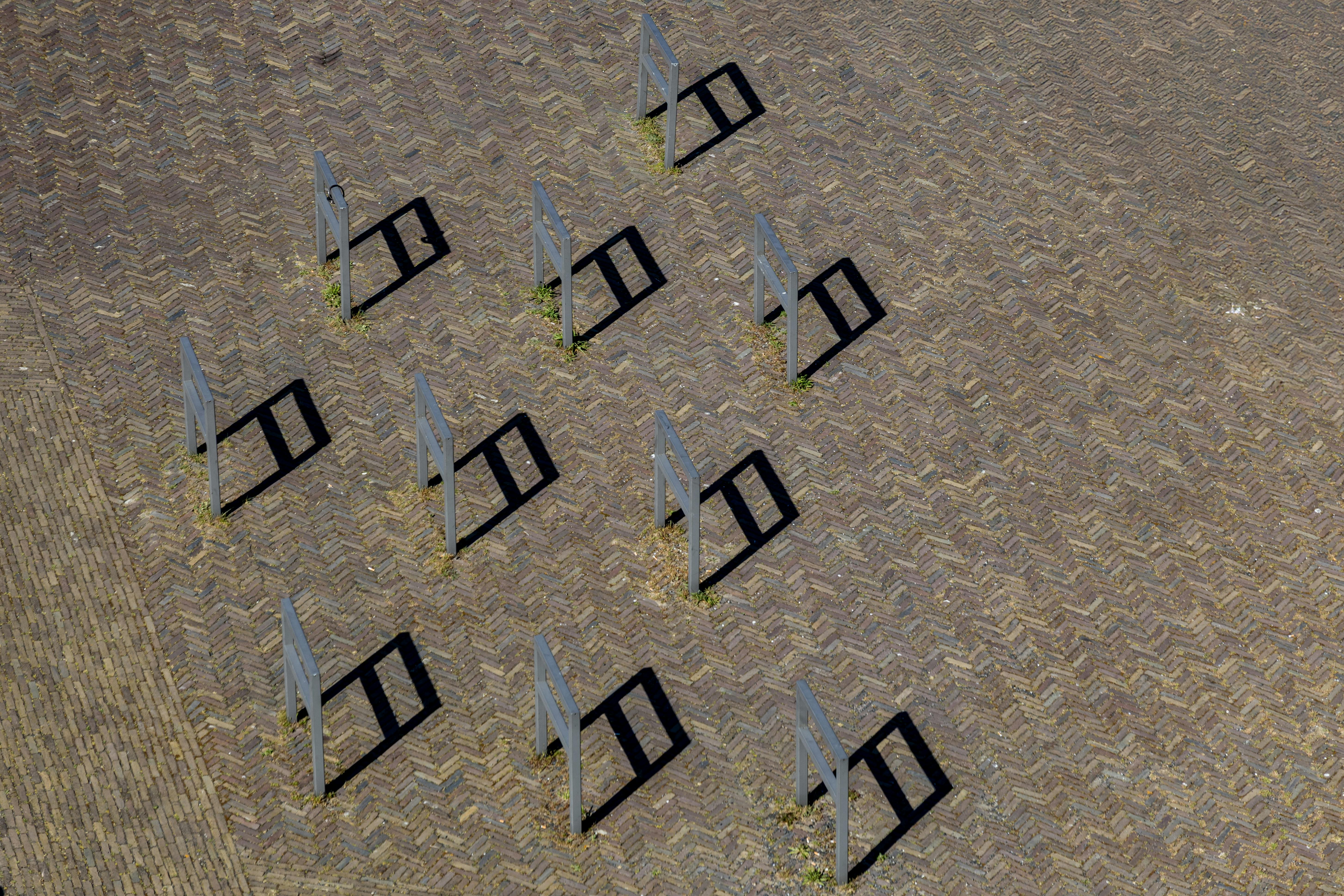 Free Aerial view of metal structures casting geometric shadows on a brick pavement. Stock Photo