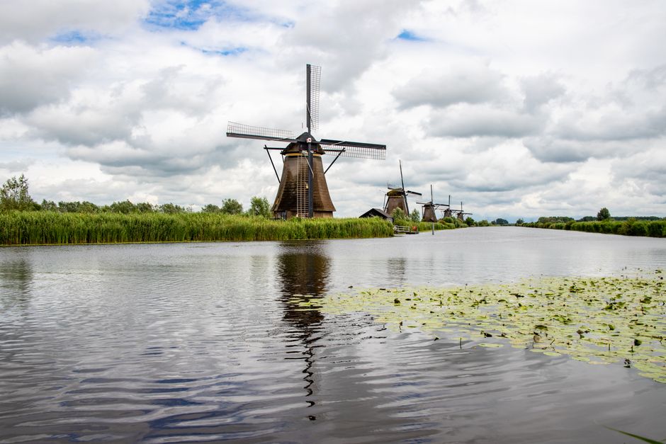 Historic Dutch windmills alongside a peaceful river under cloudy skies with grassy banks.