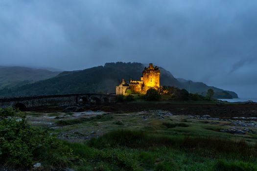 Stunning nighttime view of Eilean Donan Castle with dramatic lighting and misty surroundings.