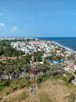 Vibrant coastal cityscape with palm trees and beach, viewed from above.