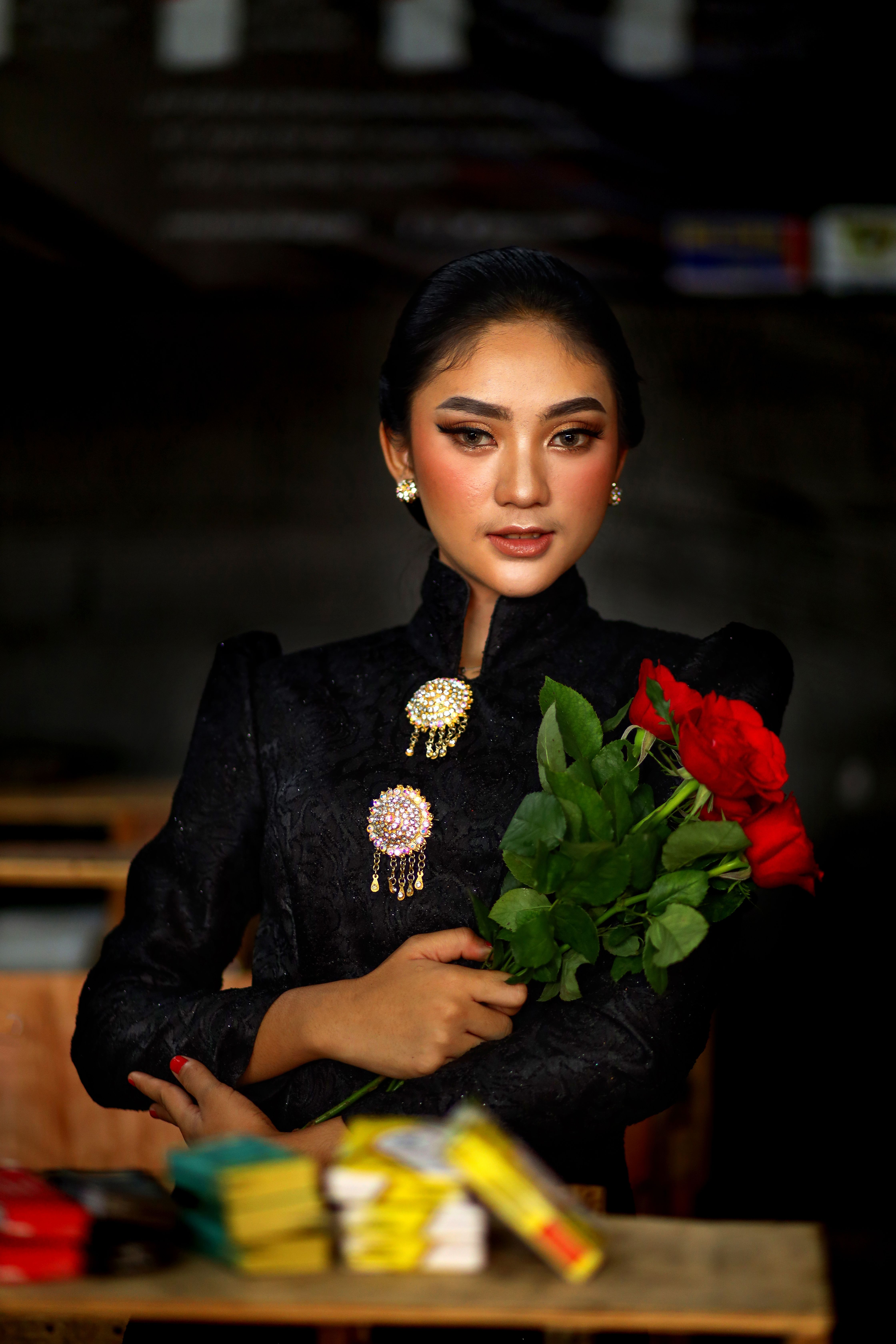 Stylish woman in black outfit holds red roses, showcasing elegance indoors in West Java, Indonesia.