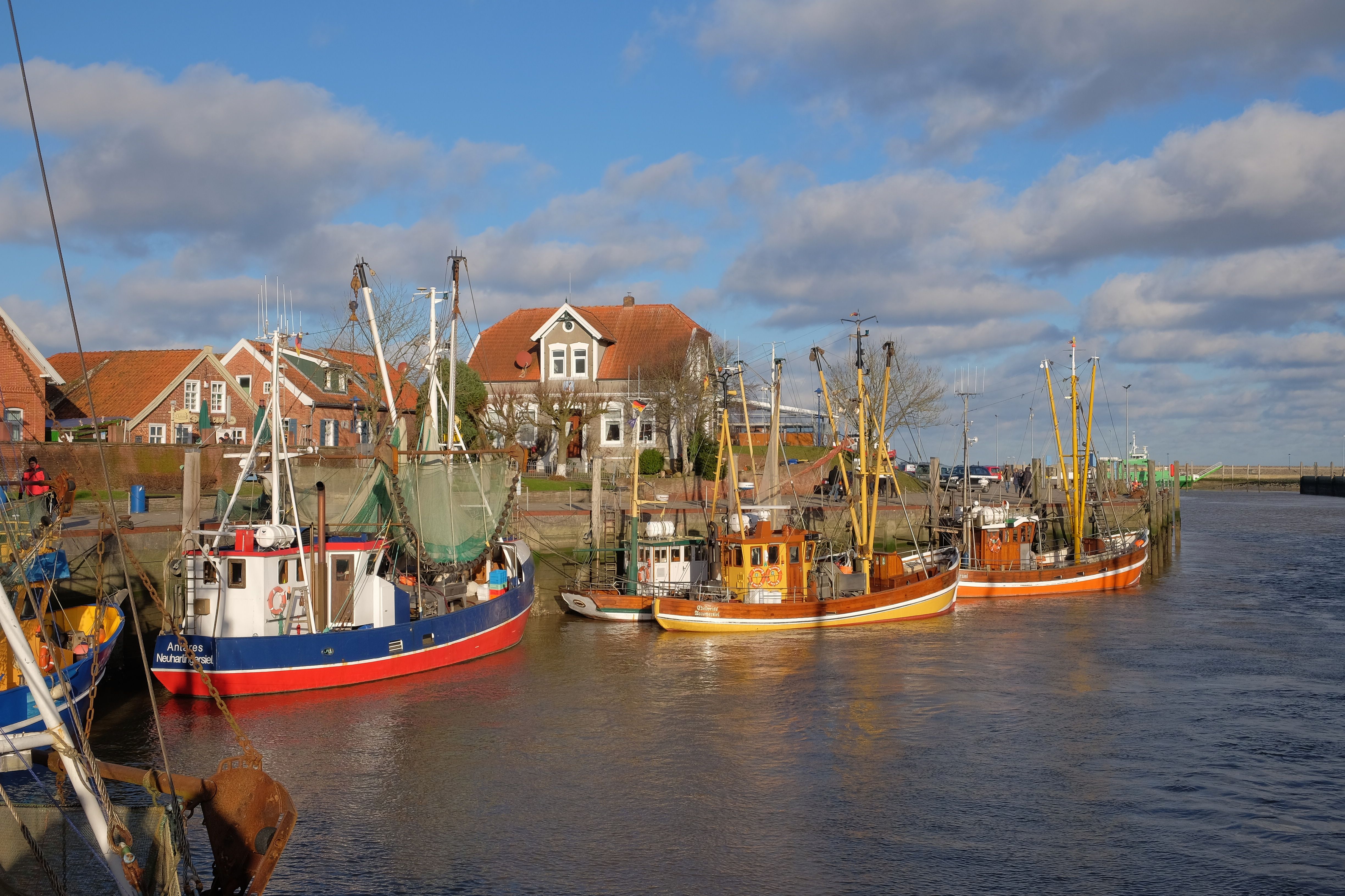 Fishing boats docked at a picturesque coastal village with traditional red-roof houses under a blue sky.
