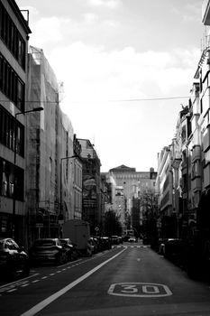 Monochrome view of a calm urban street with cars and buildings lining the sides.