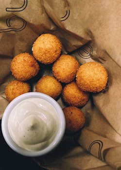 Delicious crispy cheese balls served with a creamy dipping sauce on brown paper.
