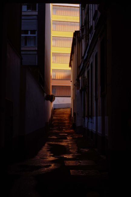 A dark alleyway with glowing windows above creates an eerie and intriguing urban scene.