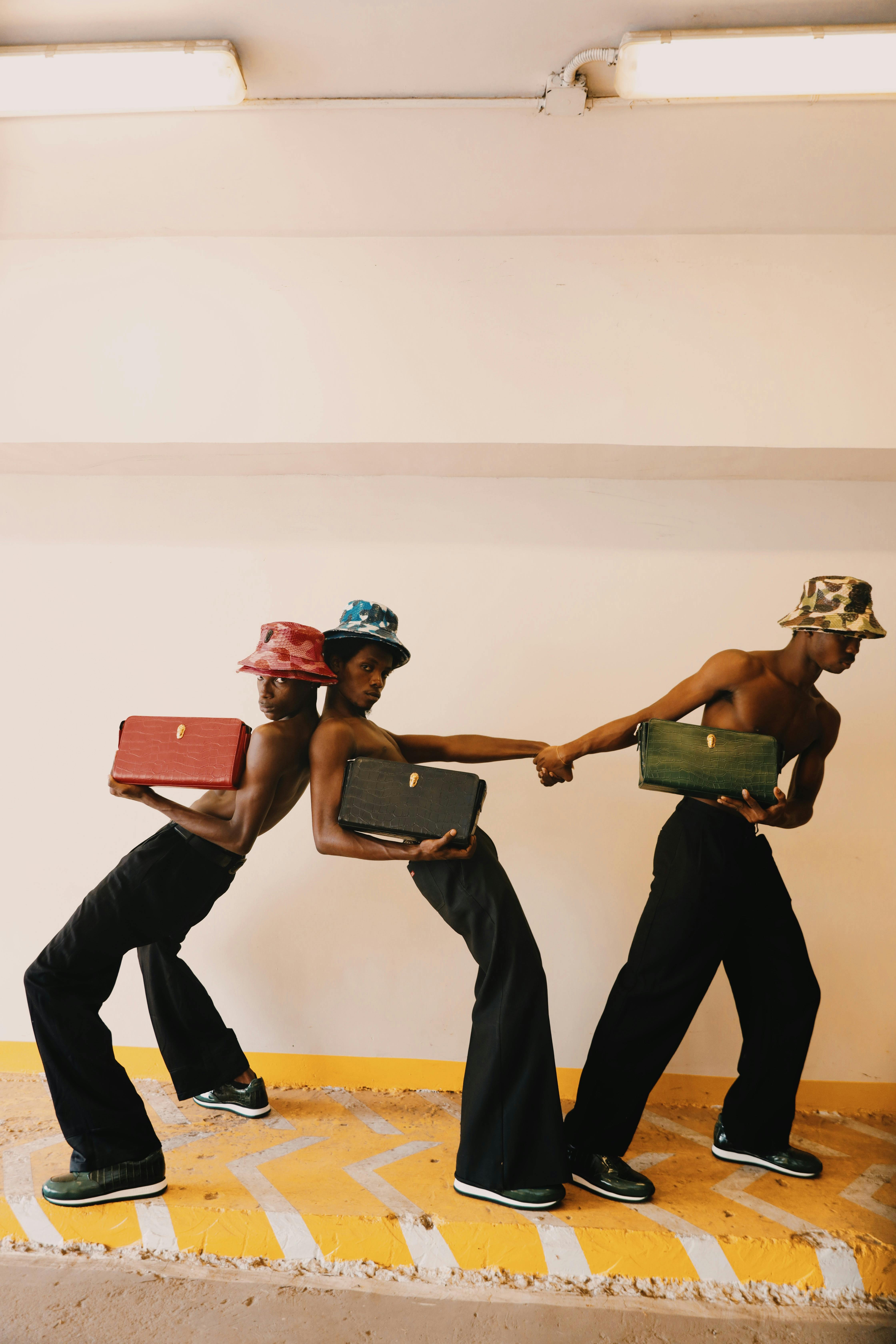 Gratis Tres jóvenes adultos con estilo, atrevidos sombreros de pescador, posan creativamente con maletas en un entorno urbano. Foto de stock