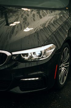 Close-up of a luxury car's headlight and hood wet with rain, showcasing elegance and detail.