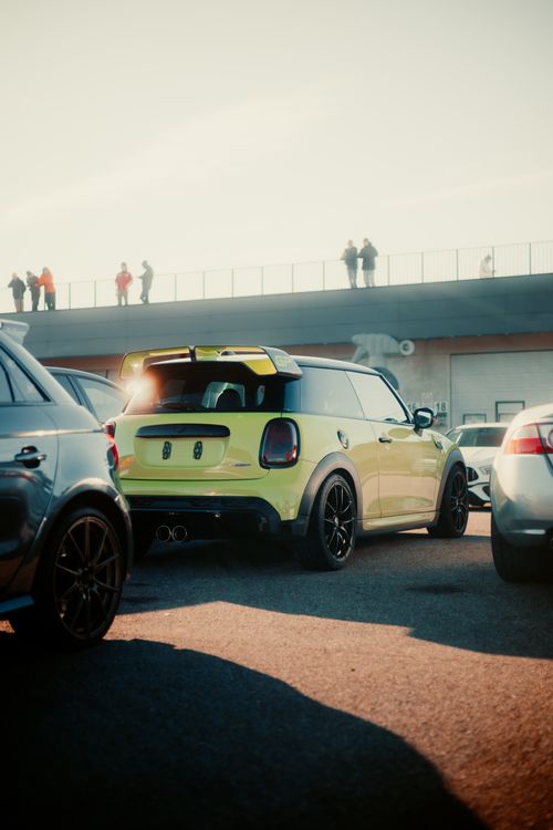 Free Yellow car parked at a racetrack, with spectators on the bridge, illuminated by sunlight. Stock Photo