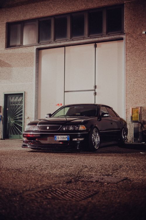 Free Stylish black car parked at night in front of a garage with urban industrial vibe. Stock Photo