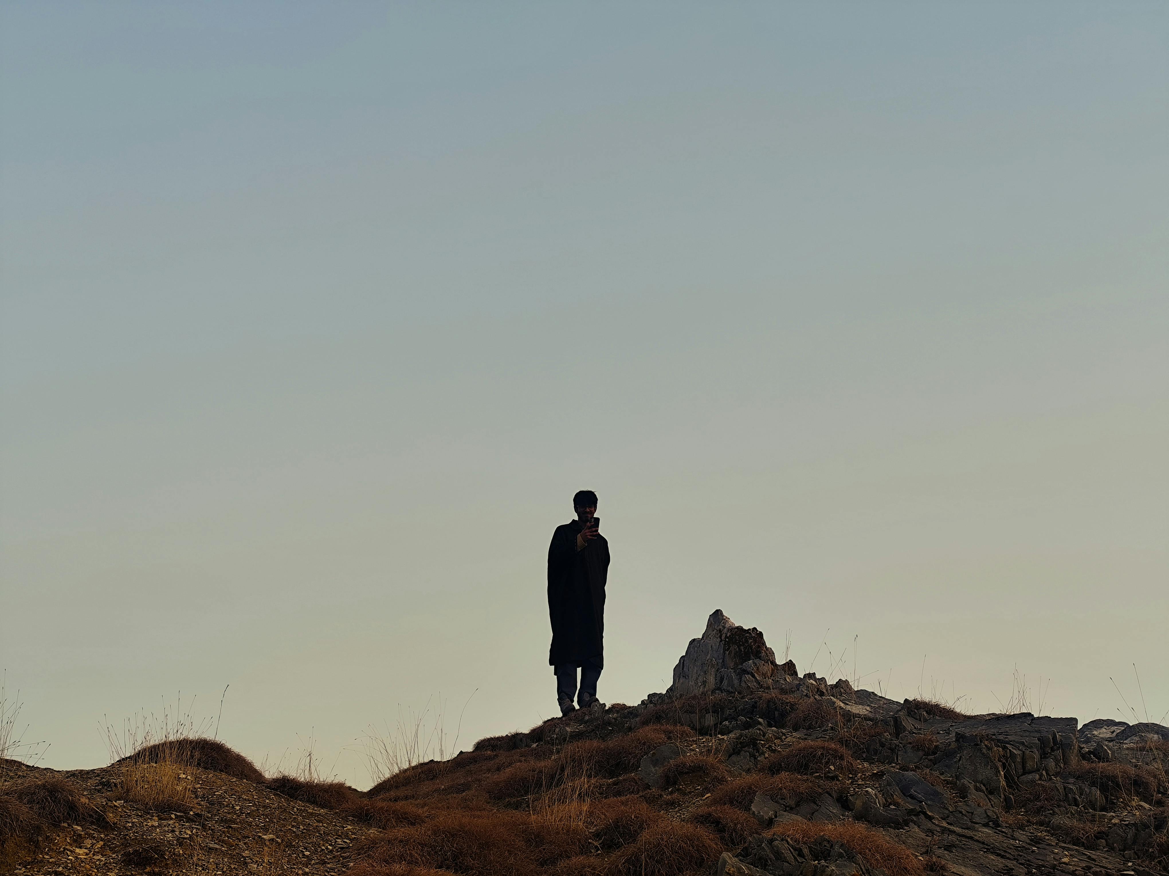 Gratis Persona in silhouette su una collina rocciosa sotto un cielo aperto. Foto a disposizione
