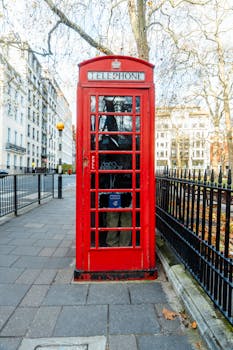 Classic red telephone booth on a city street in London, iconic symbol of British heritage.