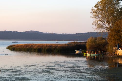 Free A peaceful lakeside view with boats and distant hills at sunset, capturing calm and tranquility. Stock Photo