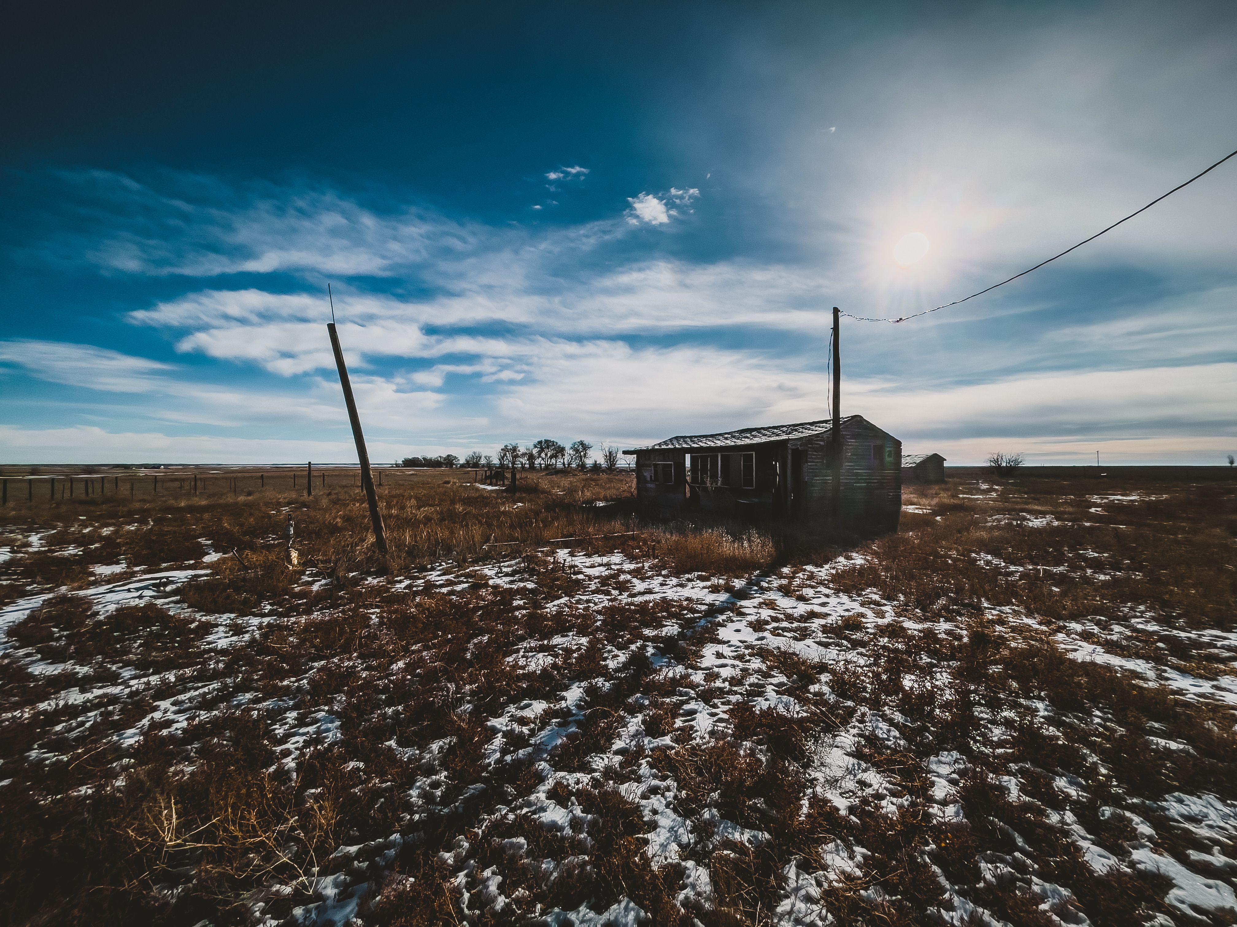 Rustic abandoned farmhouse in snowy field under bright blue sky, Cheyenne, Wyoming.
