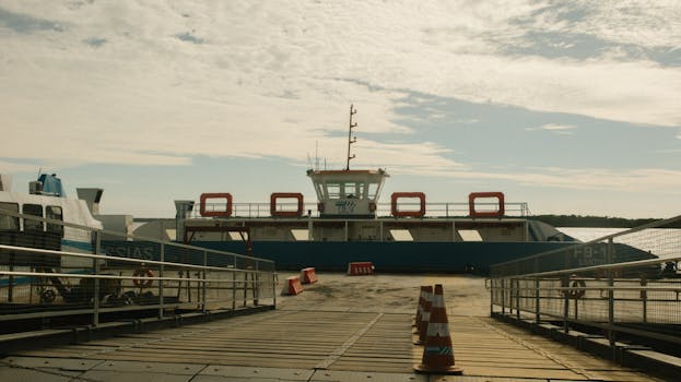 A ferry docked at a harbor under a cloudy sky with visible traffic cones.