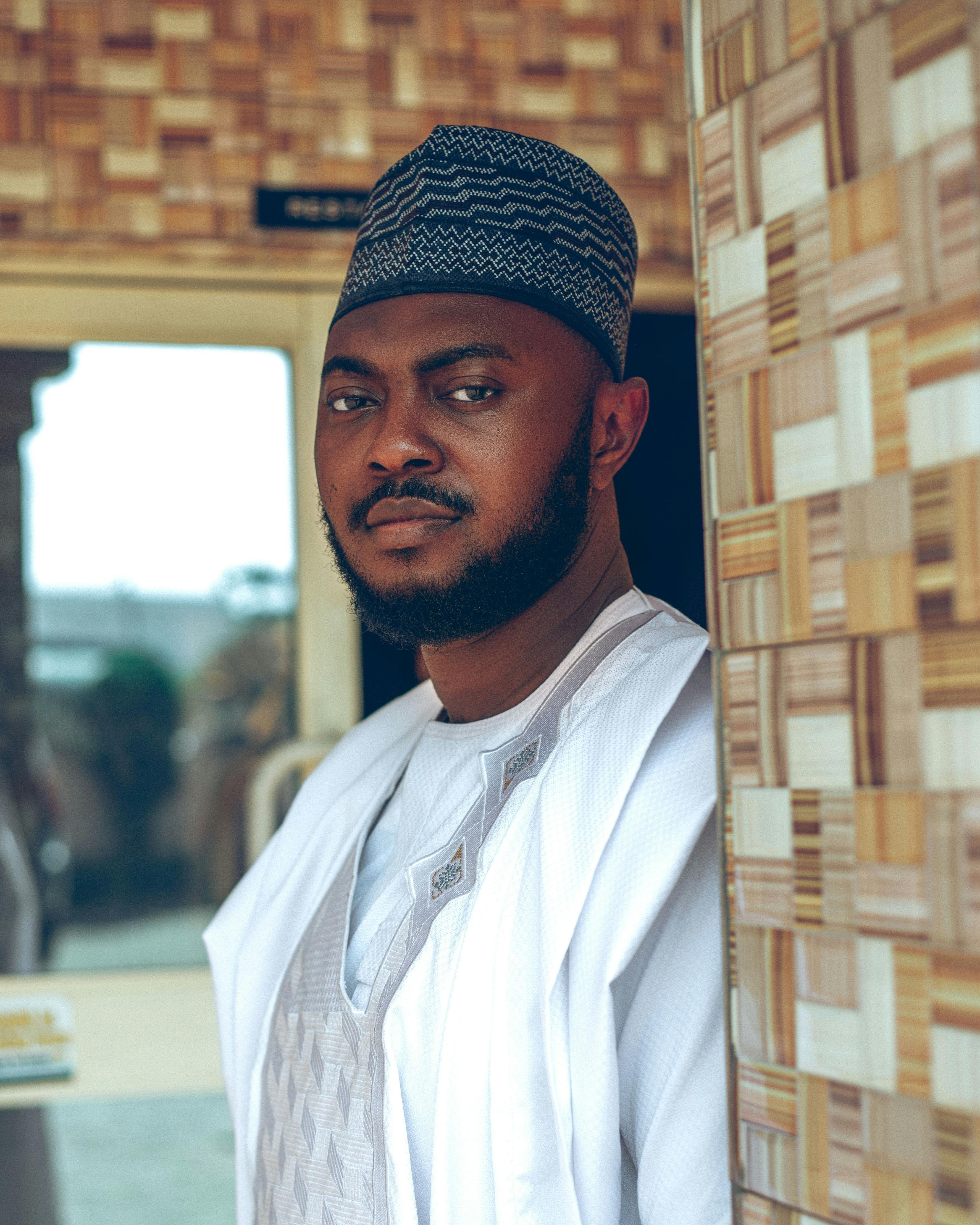 Man in traditional clothing leaning against a textured wall with a confident expression.