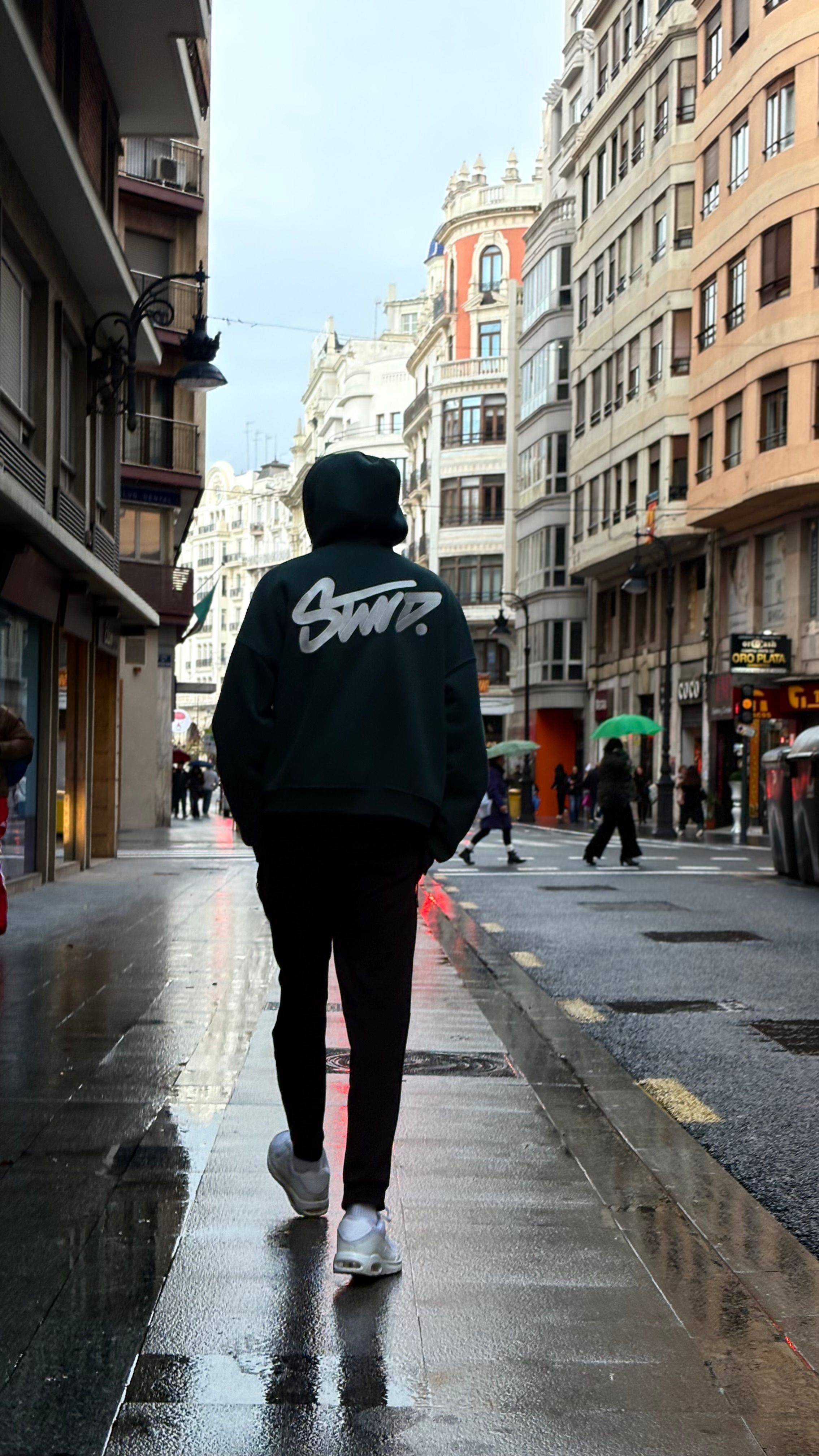Person walks down a wet city street surrounded by European architecture.