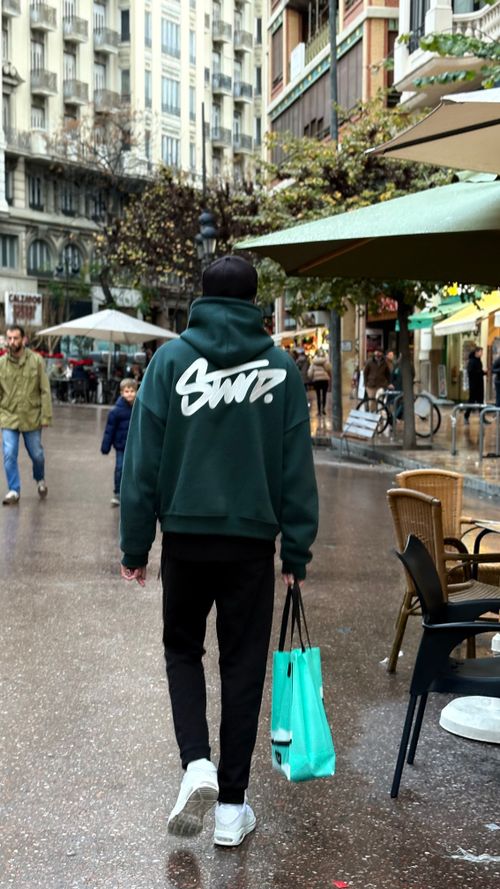 Free Person in stylish hoodie walking in a lively city street, showcasing modern urban fashion. Stock Photo