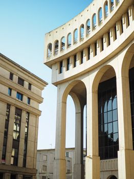 Elegant colonnaded buildings with arches under a clear blue sky, showcasing urban architecture.