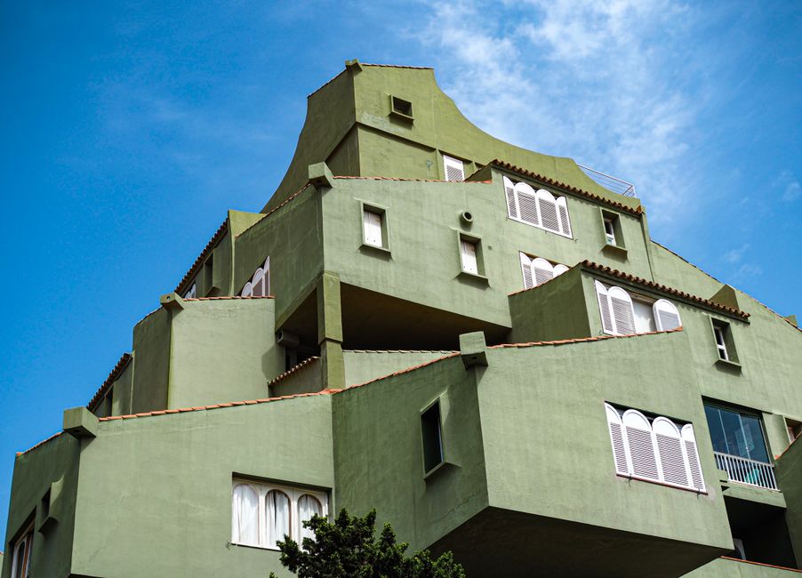 A striking green building with geometric design set against a clear blue sky, showcasing unique architecture.