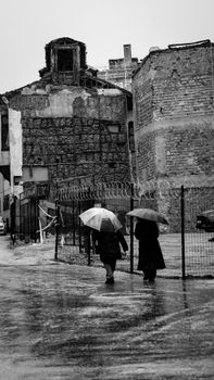 Two people with umbrellas walking beside old buildings in the rain.