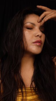 Elegant portrait of a woman in a gold top with eyes closed, serene expression.