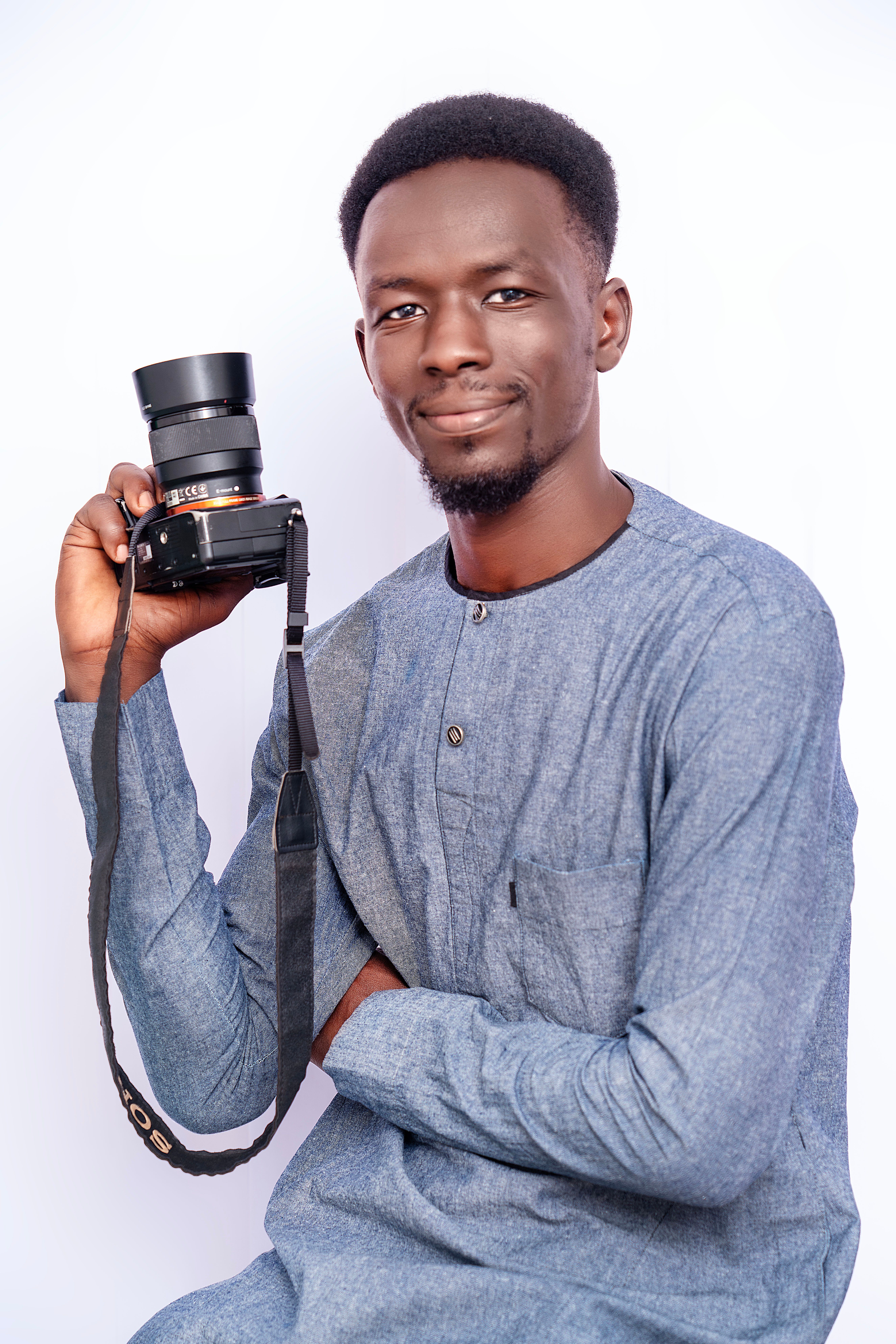 Smiling man in gray attire holding a camera, isolated on white background.