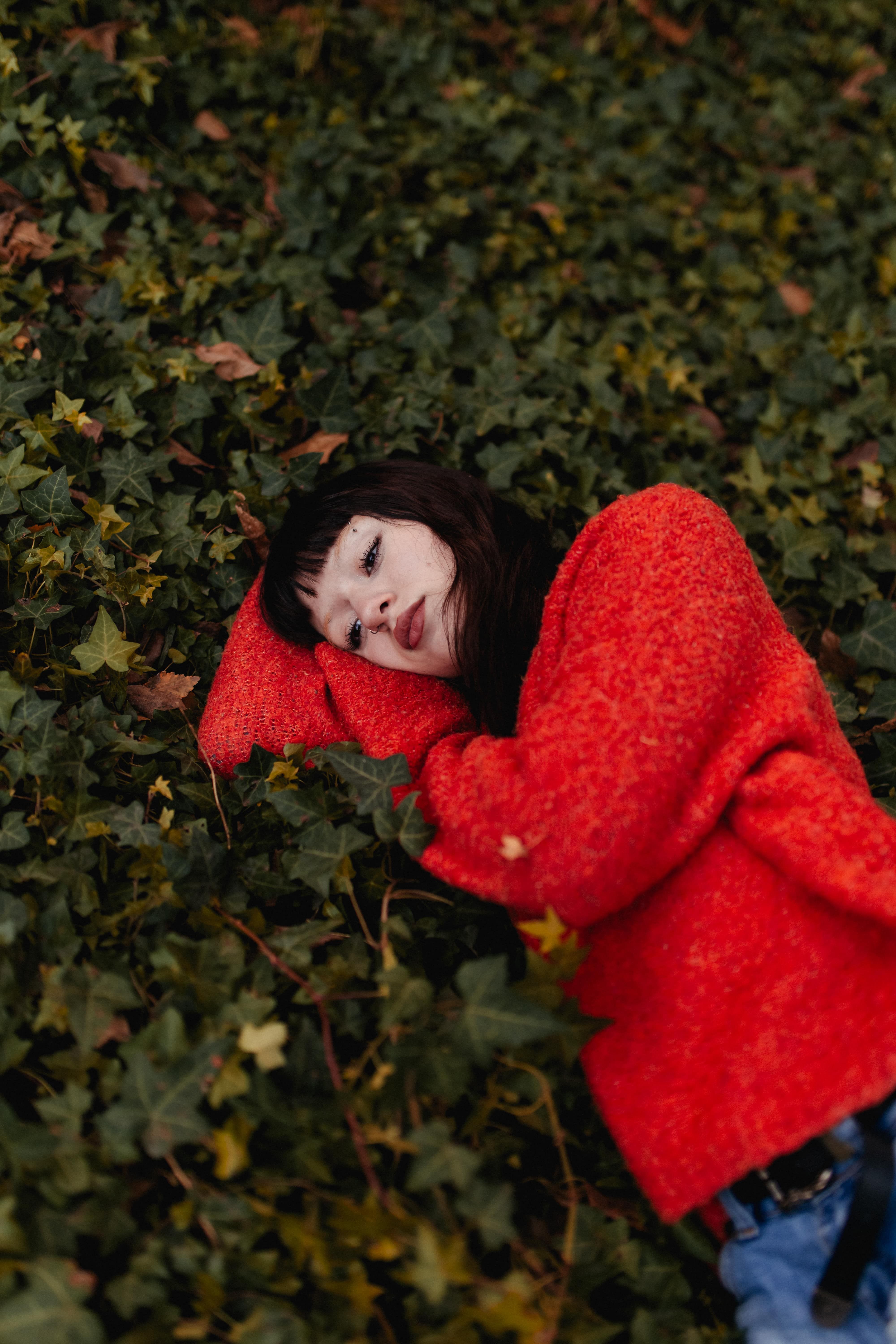 Woman in Red Sweater Lying on Green Foliage Outdoors · Free Stock Photo