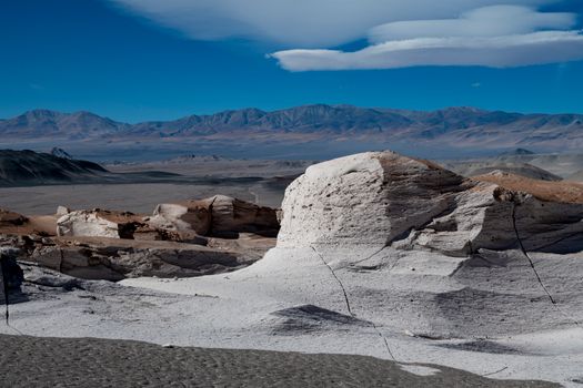 Beautiful desert scene with unique rock formations and distant mountains under a vibrant blue sky.