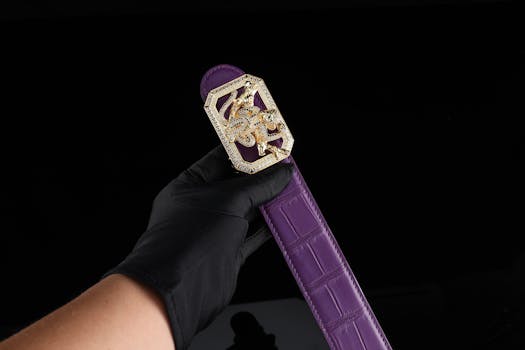 Elegant purple leather belt with an ornate gold buckle held against a dark backdrop.