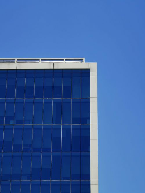 Free A modern glass building facade with blue reflections under a clear summer sky. Stock Photo