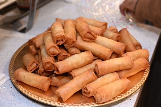 A heap of golden, crispy spring rolls displayed on a decorative tray, ready to serve.