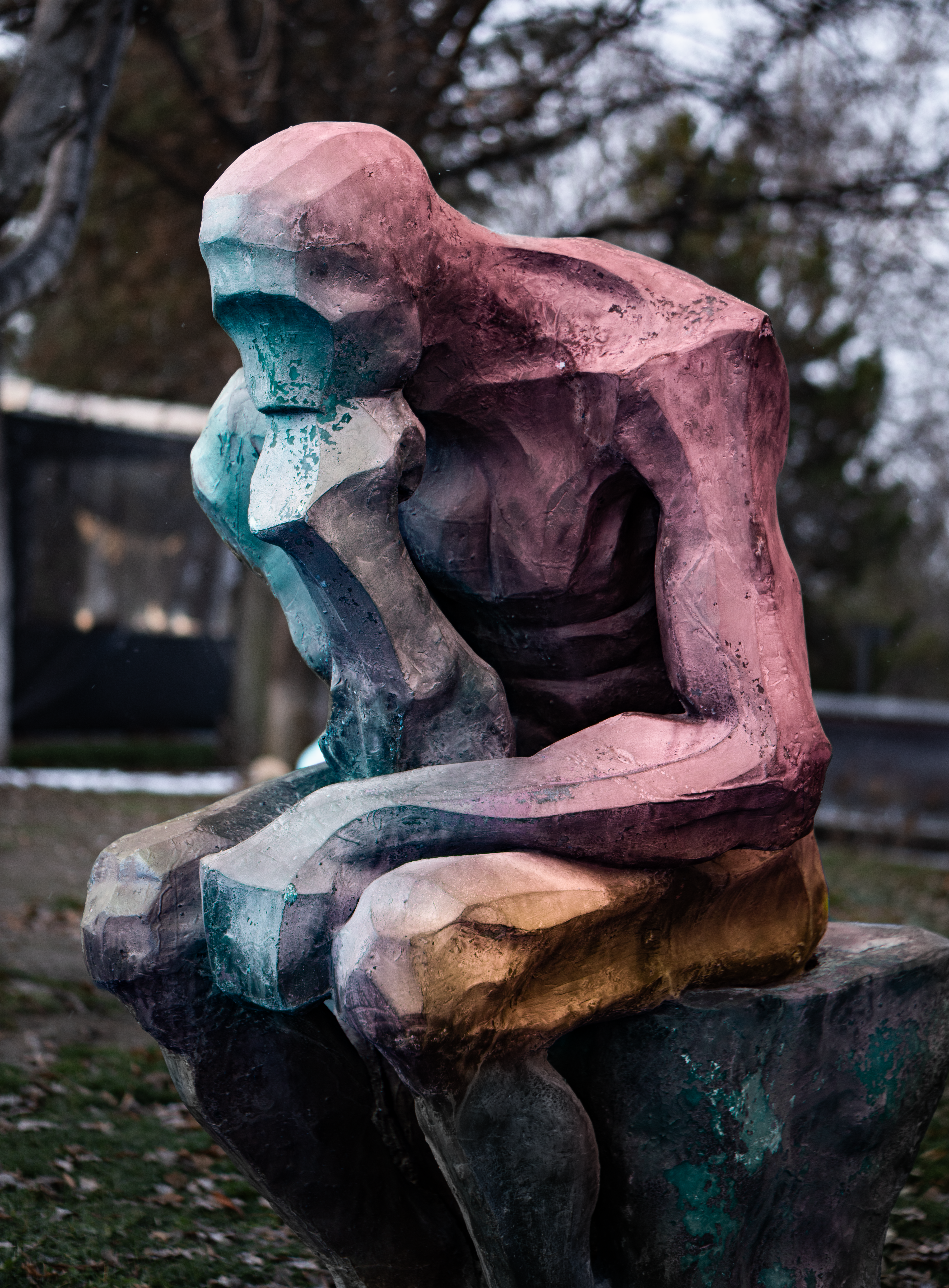 A vibrant abstract sculpture of a thinker situated in an outdoor park setting.