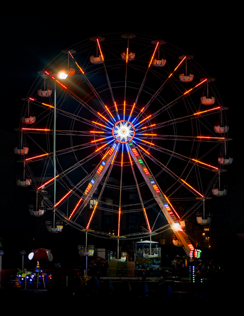 Free Illuminated Ferris wheel glowing brightly at night in a lively carnival setting. Stock Photo