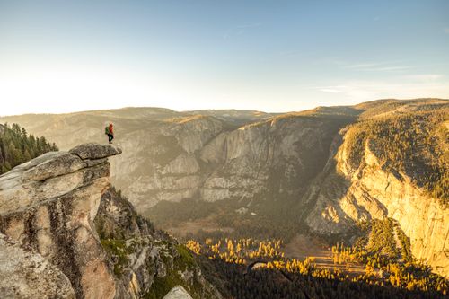 Free A lone hiker stands on the edge of a cliff in Yosemite National Park, embracing the golden fall landscape. Stock Photo