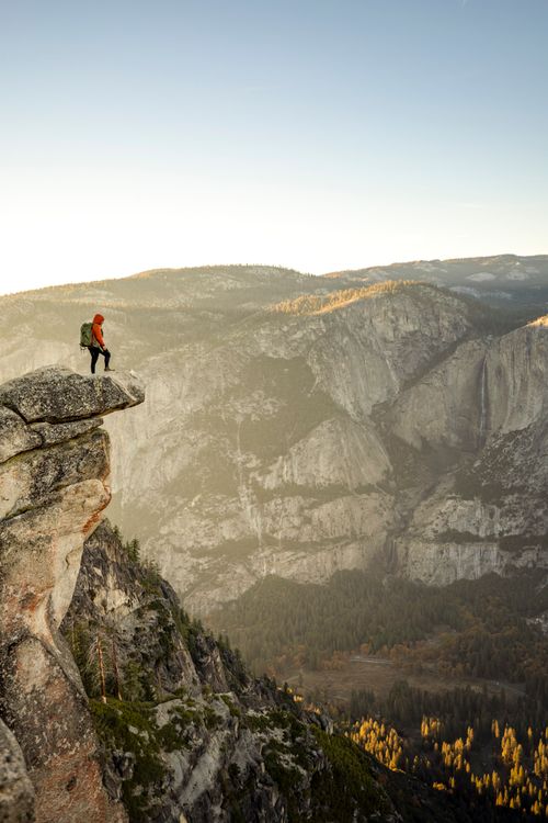 Free A lone hiker stands on a cliff edge in Yosemite National Park, overlooking a vast valley. Stock Photo