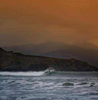 一名孤独的冲浪者迎着绚丽的橙色天空，在崎岖的海岸线上冲浪