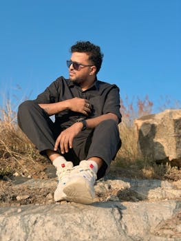 Man in casual attire sitting on rocks enjoying a sunny day outside.