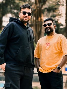 Two adult men smiling and posing outdoors wearing sunglasses in a casual setting.
