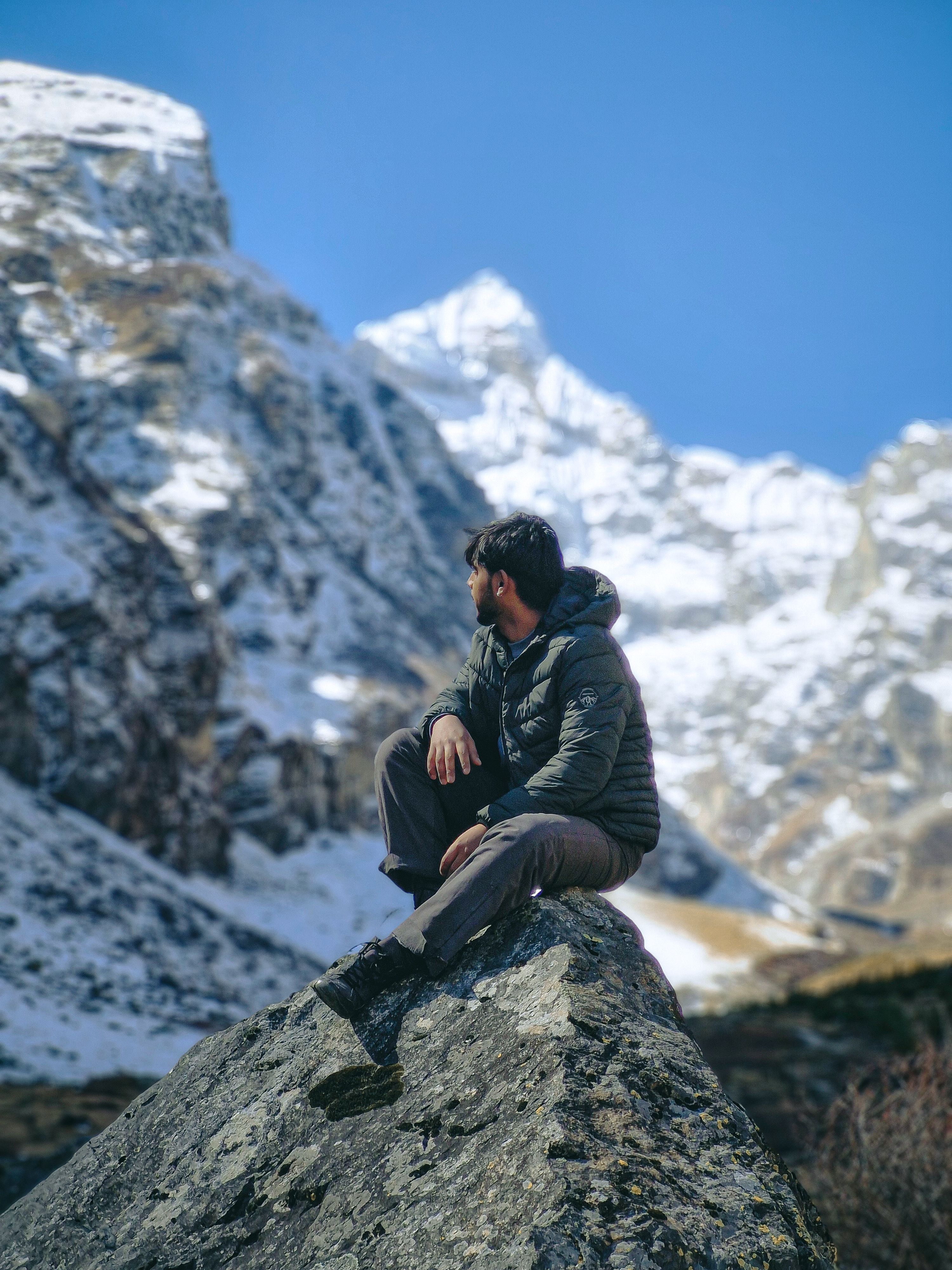 Man seated on rock in snow-covered mountain scene, embracing nature's tranquility.