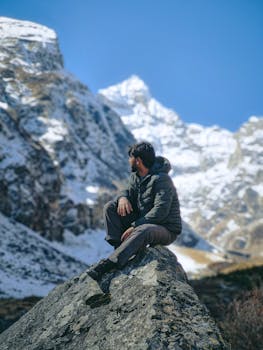 Man seated on rock in snow-covered mountain scene, embracing nature's tranquility.