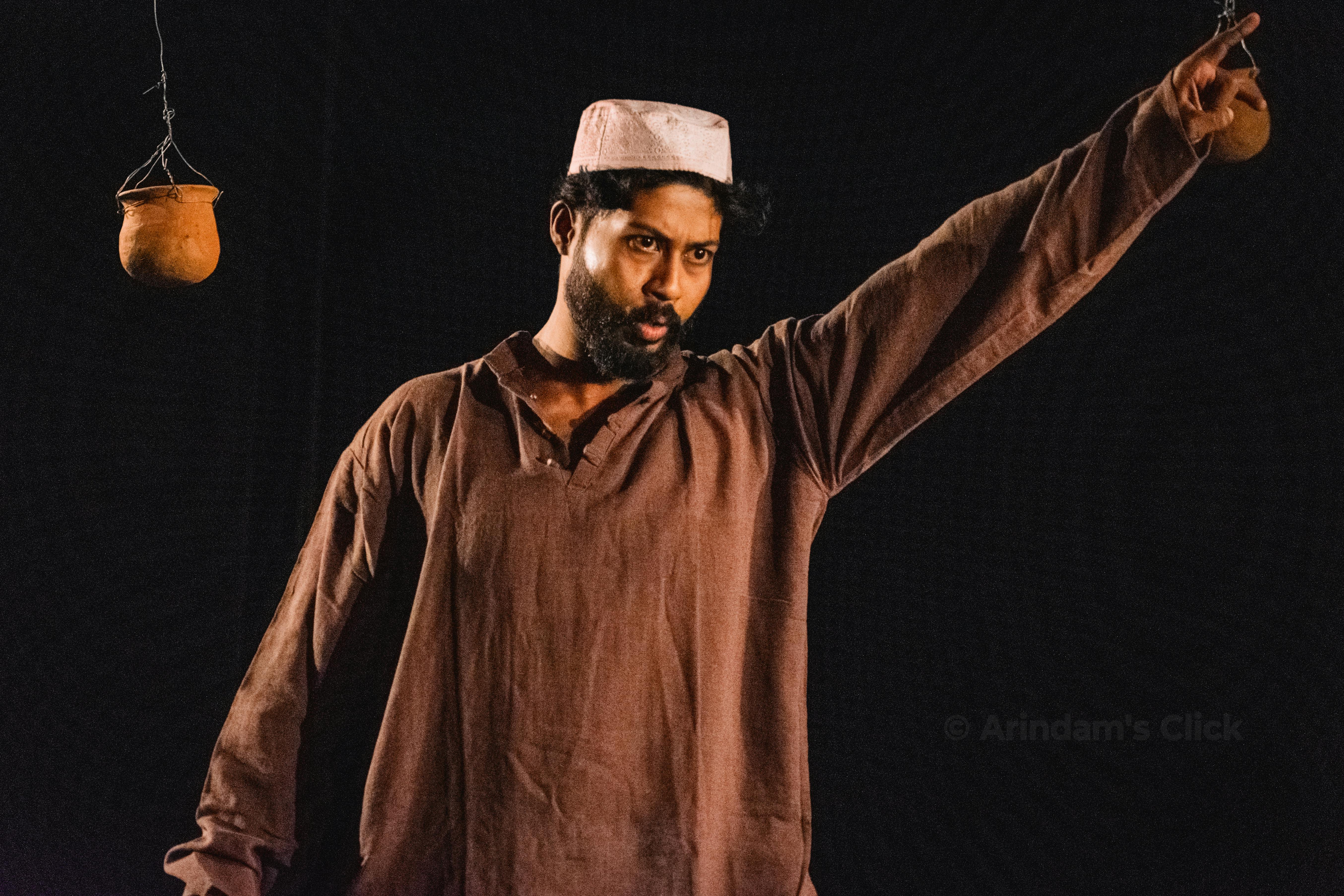 Ücretsiz Geleneksel kıyafetler giymiş bir adam, etkileyici bir ortamda asılı duran kil kaplarla işaretler yapıyor. Stok Fotoğraflar