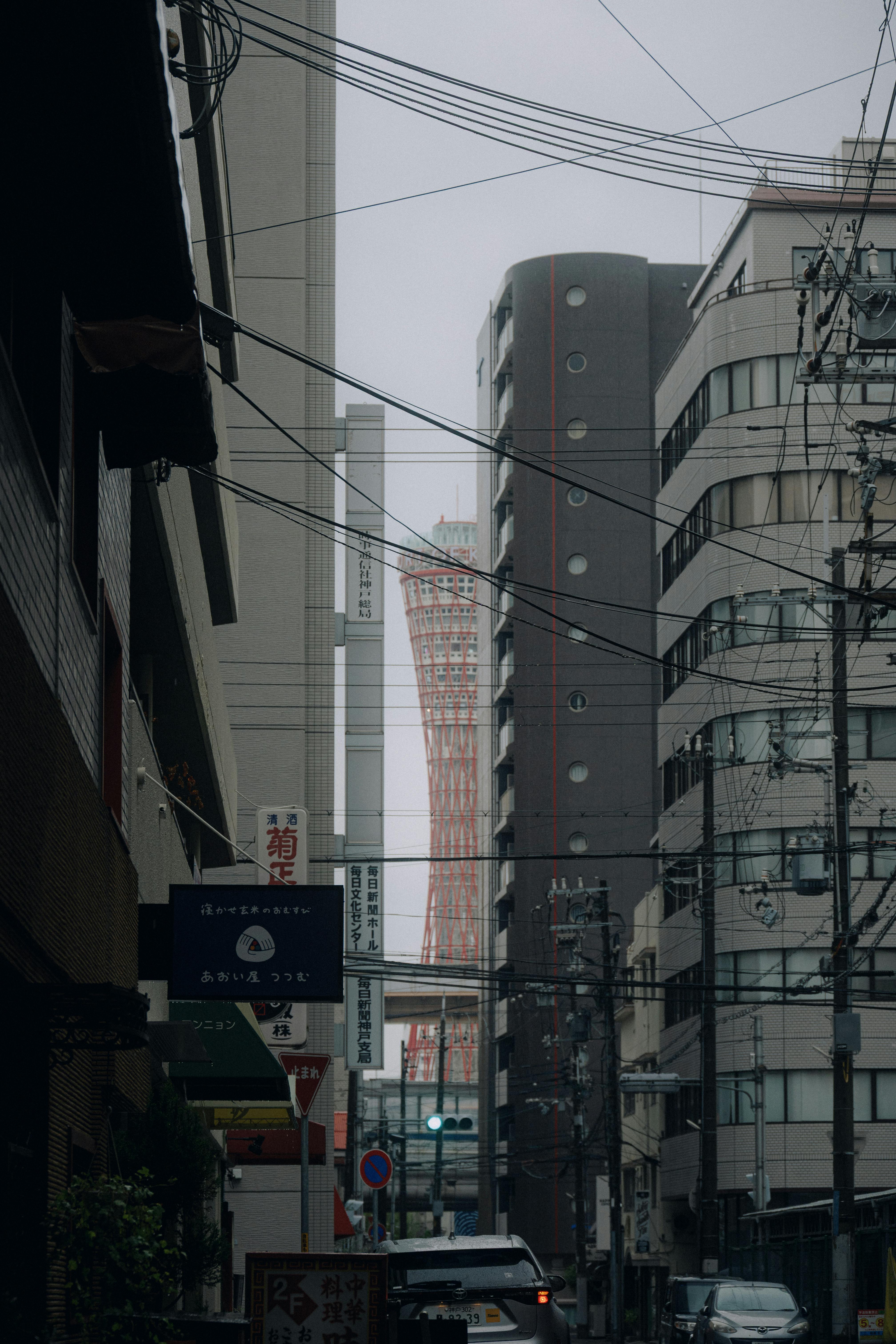 Moody urban street scene featuring the iconic Kobe Port Tower amidst buildings.
